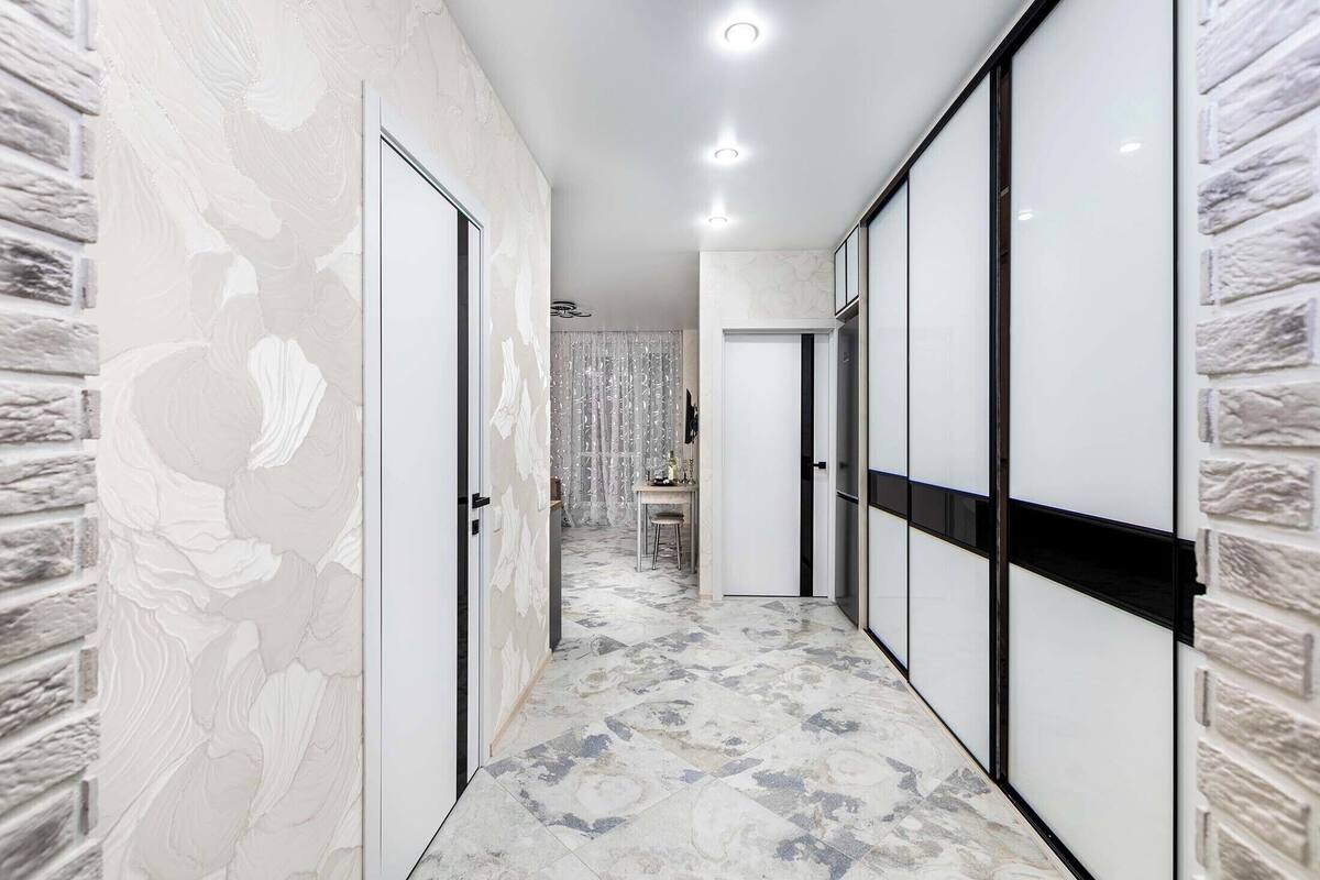 Um corredor com paredes padronizadas, piso ladrilhado e uma porta que dá para um quarto.