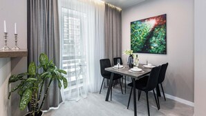 Un comedor moderno con una mesa dispuesta para cuatro personas, sillas negras, una planta en maceta y un cuadro abstracto grande en la pared.