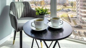 Una habitación con un ventanal grande, un sillón tapizado gris y una mesita redonda con dos tazas y platillos blancos.
