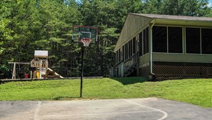A basketball court with a hoop, a playground structure, and a building with large windows.