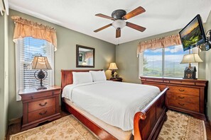 Ein Schlafzimmer mit einem hölzernen Bett, zwei Nachttischen, einem Deckenventilator und einem großen Fenster mit Jalousien.