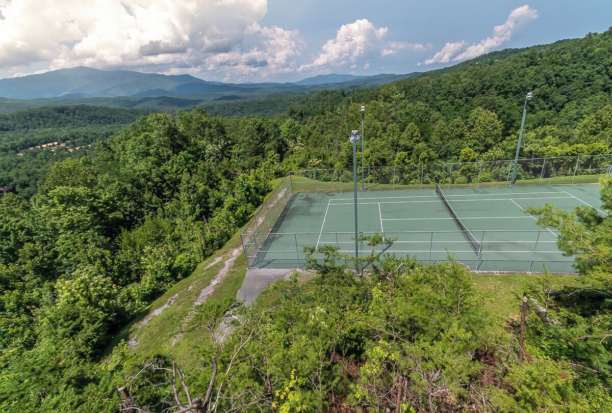 Un court de tennis entouré d’une végétation luxuriante, avec des montagnes en arrière-plan.