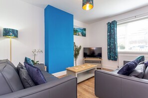 Ein modernes Wohnzimmer mit blauer Akzentwand, einem Flachbildfernseher, einem Couchtisch und zwei grauen Sofas.