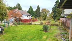A grassy backyard with a house, a wooden fence, and trees. - T2 apartment 44 m2, self-contained. (Kesseldorf)