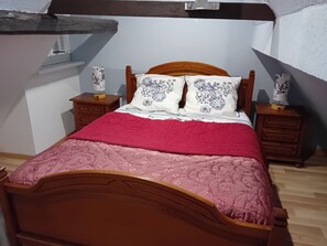 Ein Schlafzimmer mit einem hölzernen Bett, Bettwäsche in Rot und Pink, zwei Nachttischen mit Lampen und einer weißen Wand.