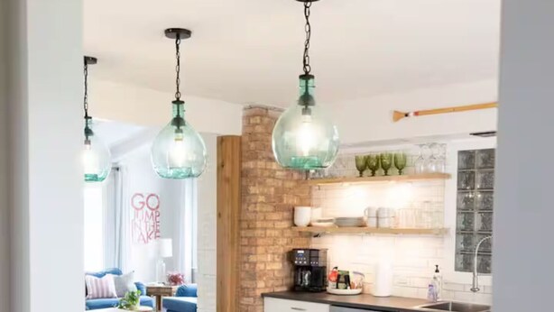 A modern kitchen with a central island, bar stools, hanging pendant lights, and a brick accent wall.