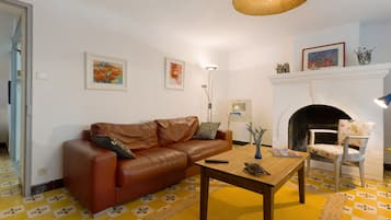 Ein Wohnzimmer mit braunem Ledersofa, einem Holztisch, einem Kamin und einem gemusterten Boden.