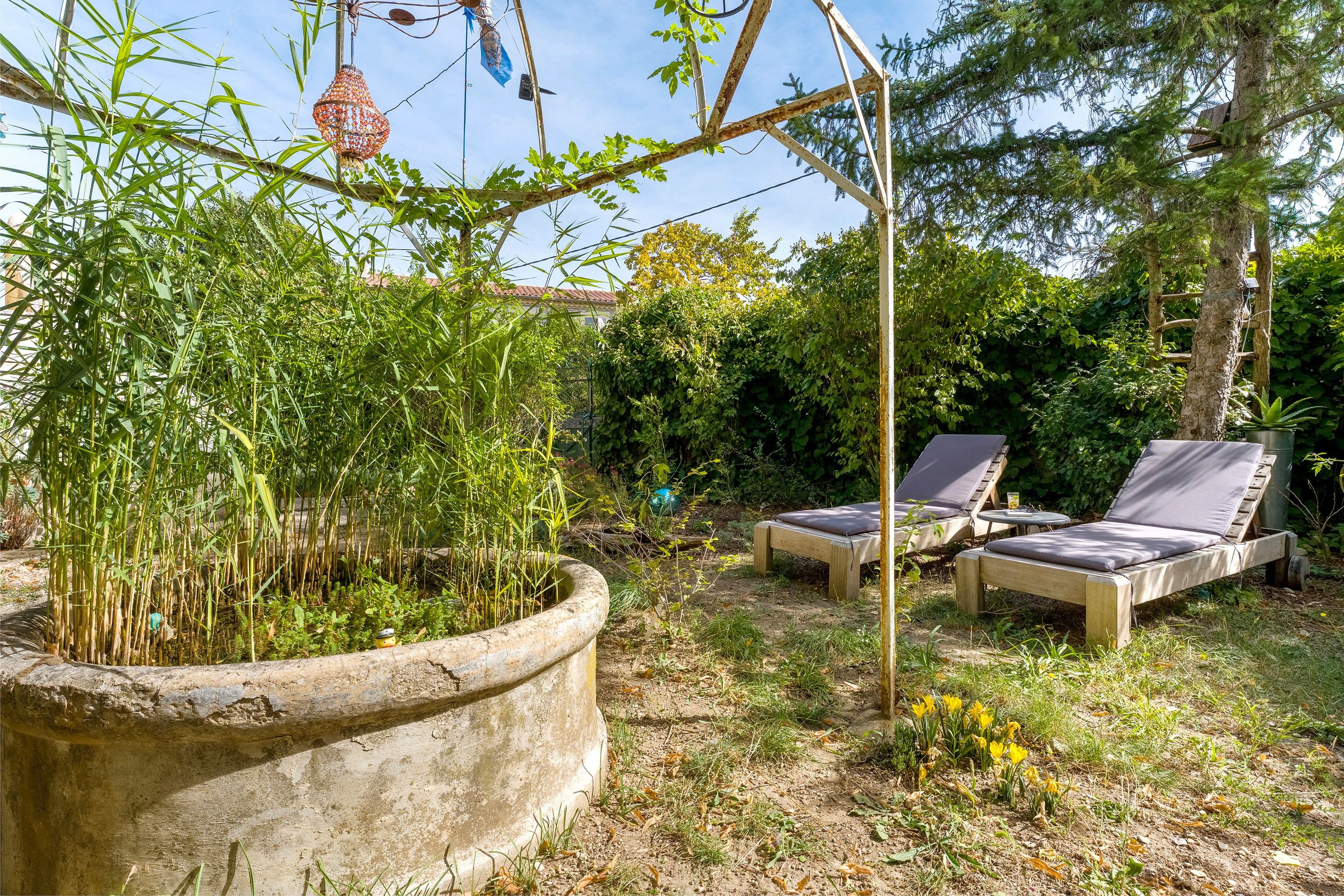Ein Garten mit einem Betonpflanzgefäß, zwei Liegestühlen und einer Pergola.