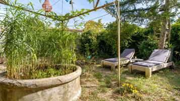 Ein Garten mit einem Betonpflanzgefäß, zwei Liegestühlen und einer Pergola.