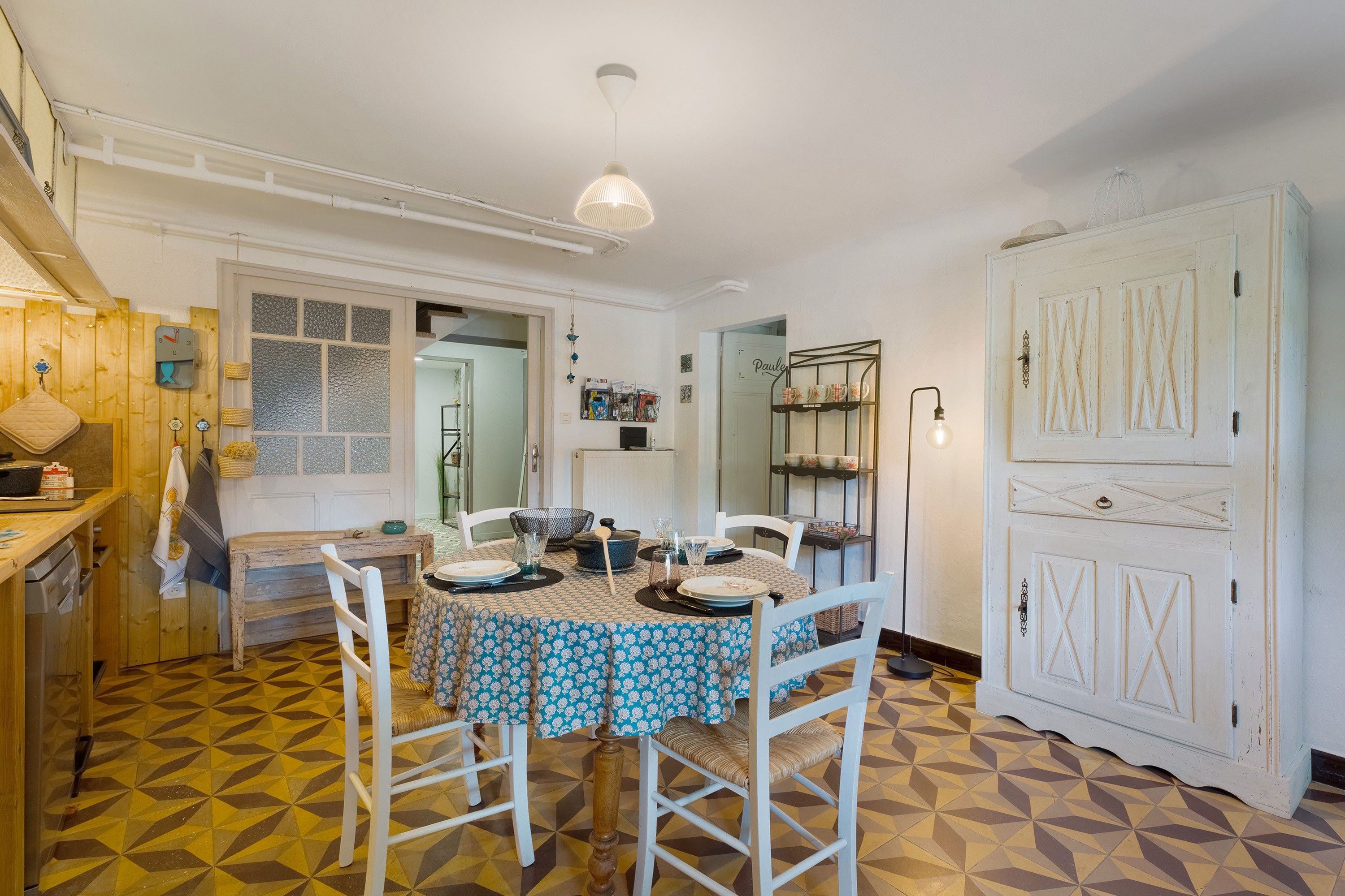 A dining area with a table set for four, chairs, a hanging light fixture, and a patterned floor.