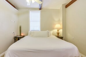 A bedroom with a large bed, a nightstand with a lamp, a window with blinds, and a ceiling fan. - Walkable Studio 1 Mi to Riverwalk & Dtwn Bradenton (Bradenton)