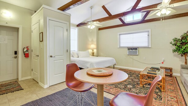 Une pièce de taille modeste comprenant un lit, deux chaises, une petite table, un ventilateur de plafond et une fenêtre.