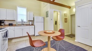 Une cuisine avec des meubles blancs, un réfrigérateur, une cuisinière et un coin repas comprenant une table ronde et deux chaises.