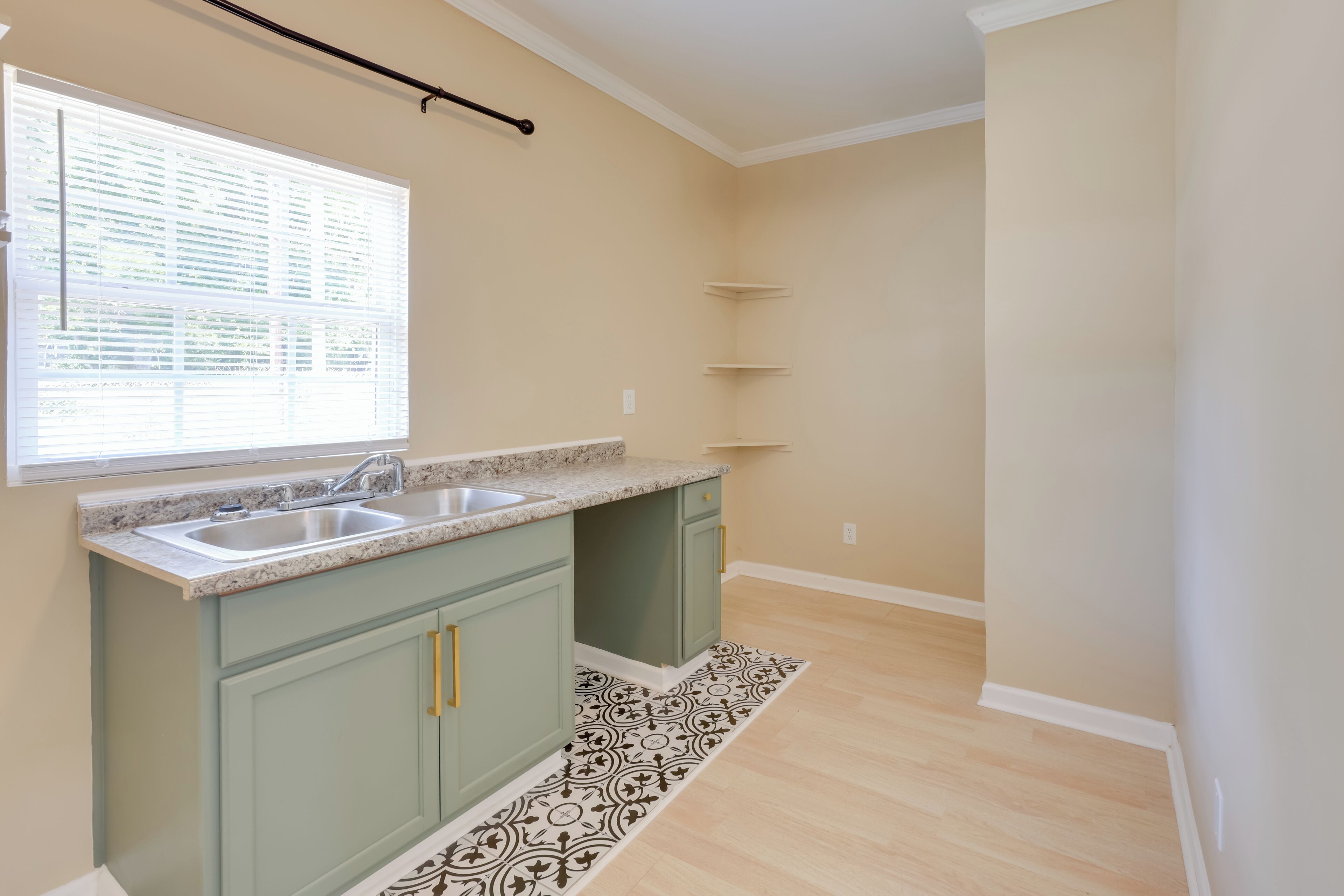 A kitchen with two sinks, green cabinets, a patterned rug, and a window with blinds.