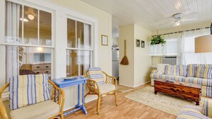Una sala de estar acogedora con piso de madera, una mesa azul, sillas de mimbre, un sofá a rayas y una mesa de centro de madera.