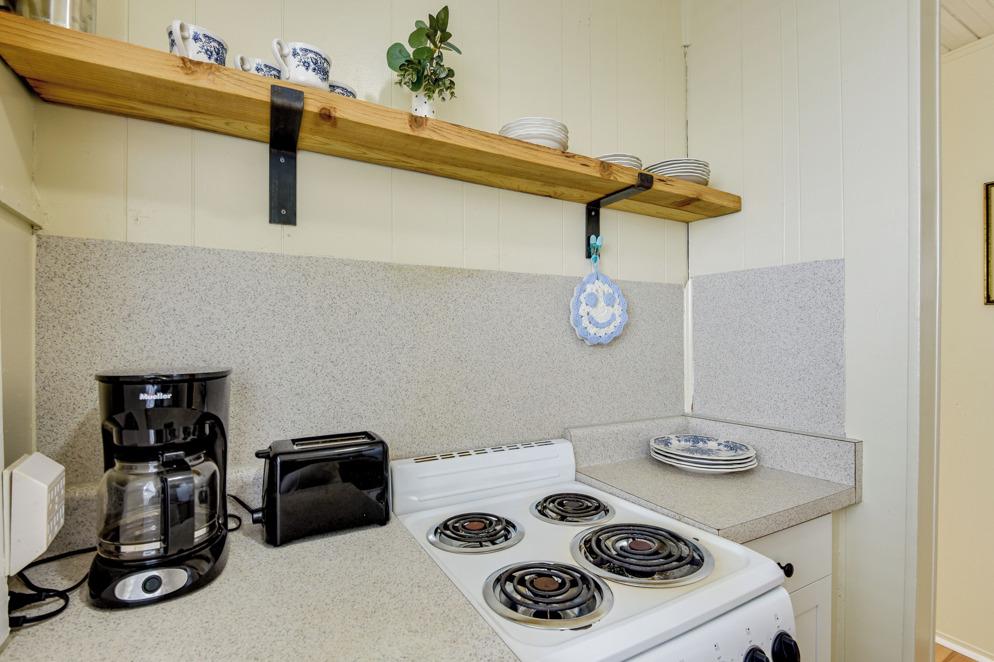A kitchen with a white stove, a coffee maker, a toaster, and a hanging pot holder.