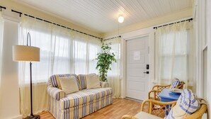 Una sala de estar acogedora con un sofá a rayas, una mesita, sillas de mimbre, una lámpara de pie y una planta en maceta.