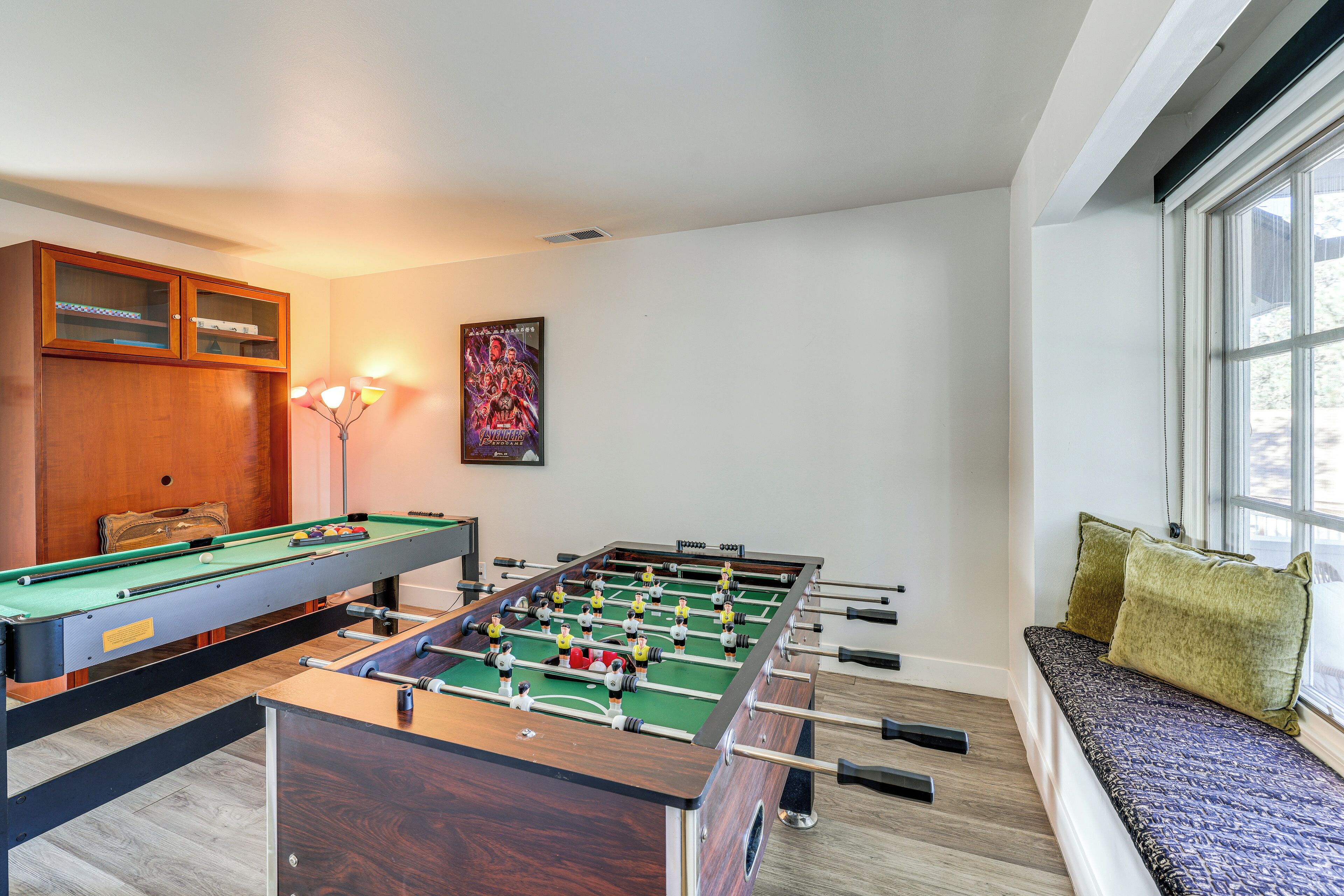 Una habitación con mesa de fútbol, mesa de billar y un sofá junto a una ventana.