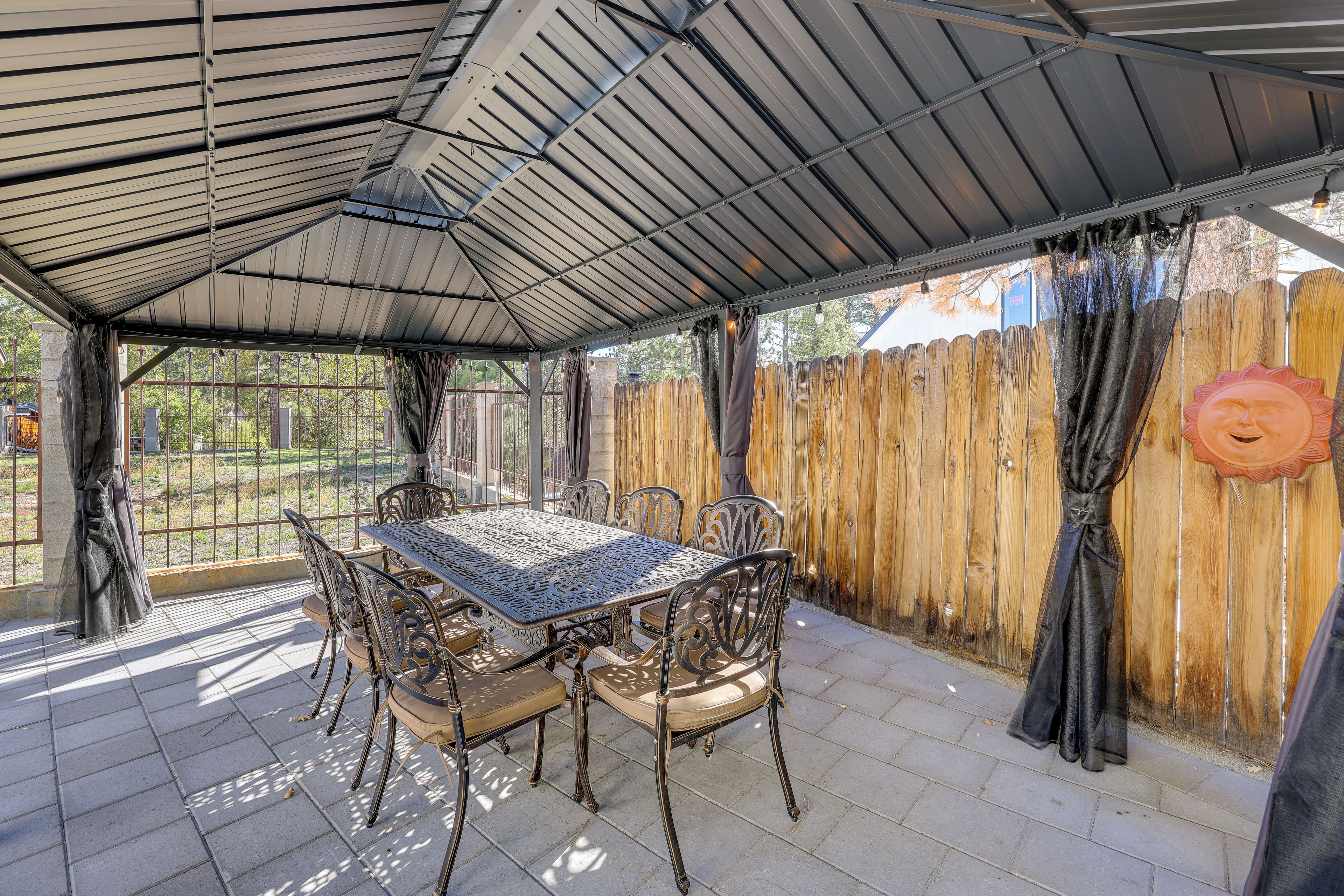 A covered patio with a table and chairs, a wooden fence, and a view of the outdoors.