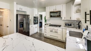 Une cuisine moderne avec des meubles blancs, un réfrigérateur en acier inoxydable, un four à micro-ondes, une cuisinière et un évier.