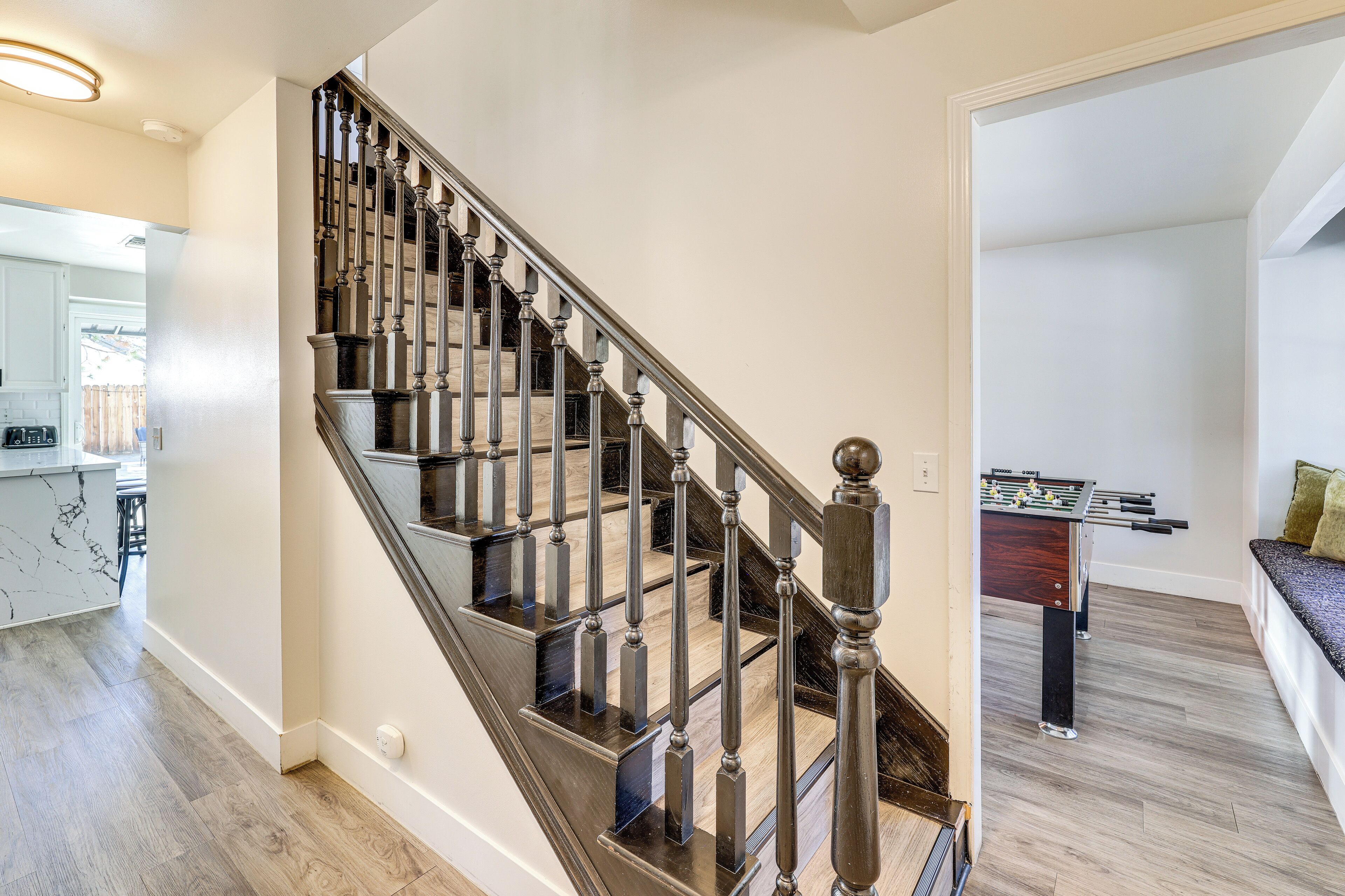 A modern staircase with a dark finish and glass railings, leading to a living area with a foosball table and a seating area with a cushioned bench.