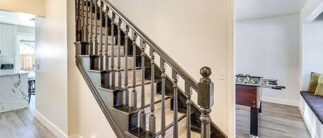 A modern staircase with a dark finish and glass railings, leading to a living area with a foosball table and a seating area with a cushioned bench.