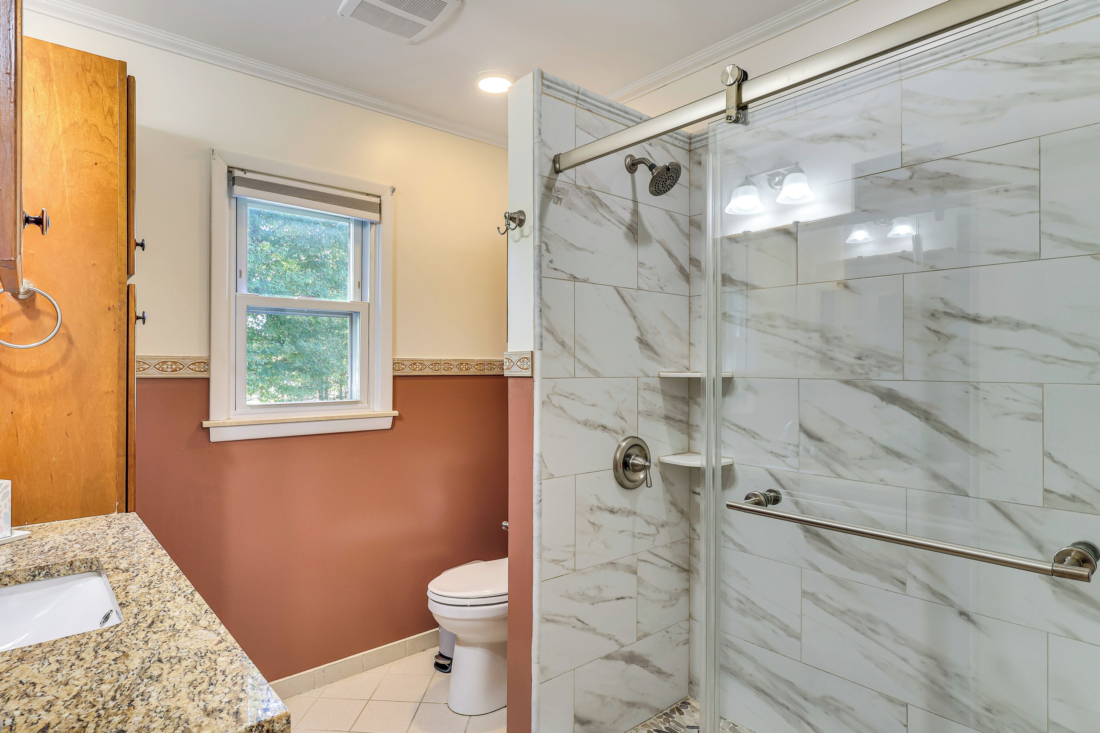 A bathroom with a marble shower, a toilet, and a sink.