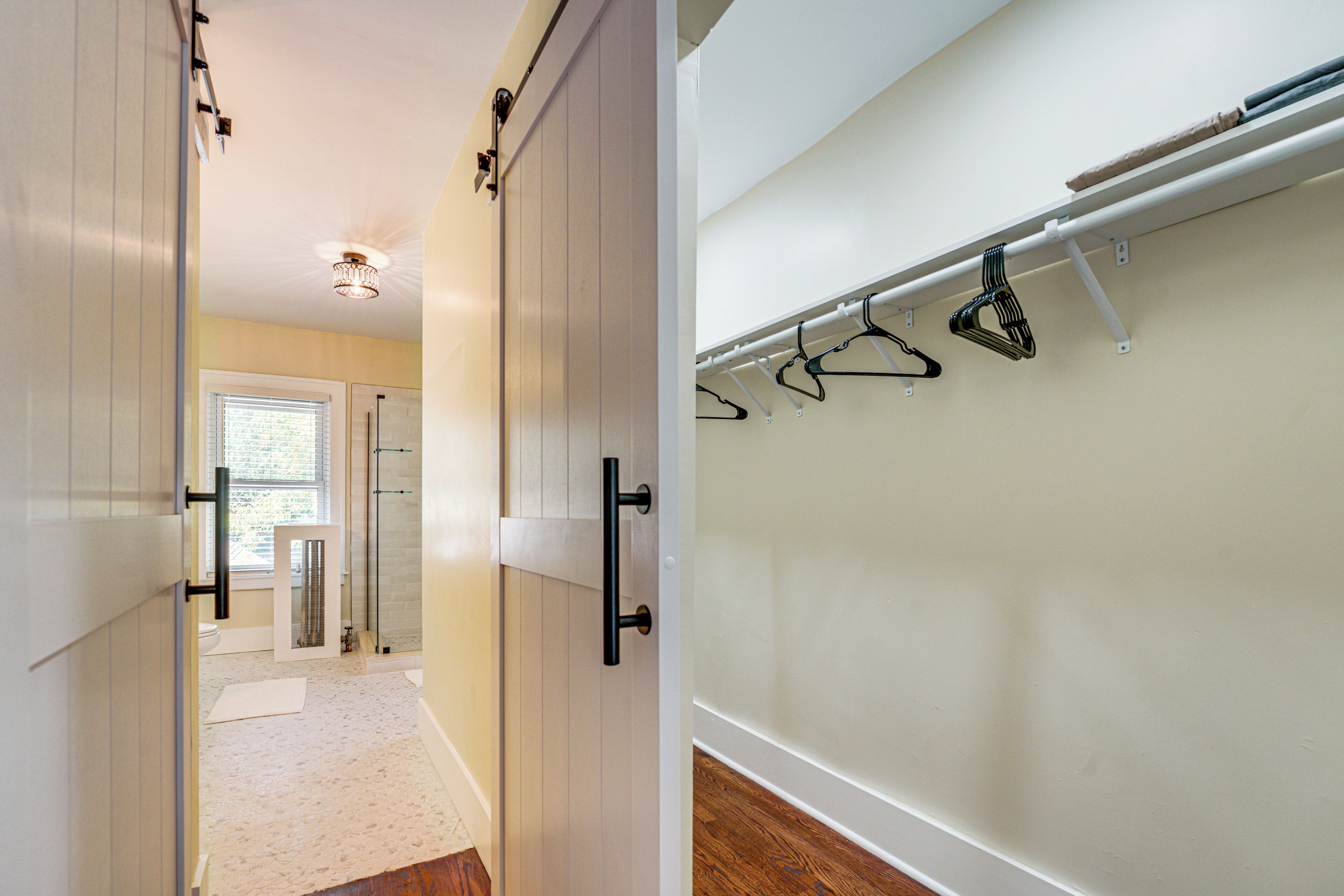 A hallway with a sliding door leading to a bathroom, a coat rack with hangers, and a wooden floor.