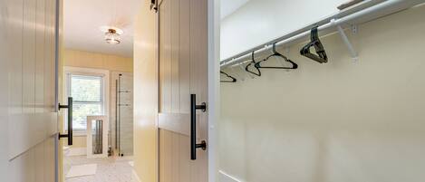 A hallway with a sliding door leading to a bathroom, a coat rack with hangers, and a wooden floor.