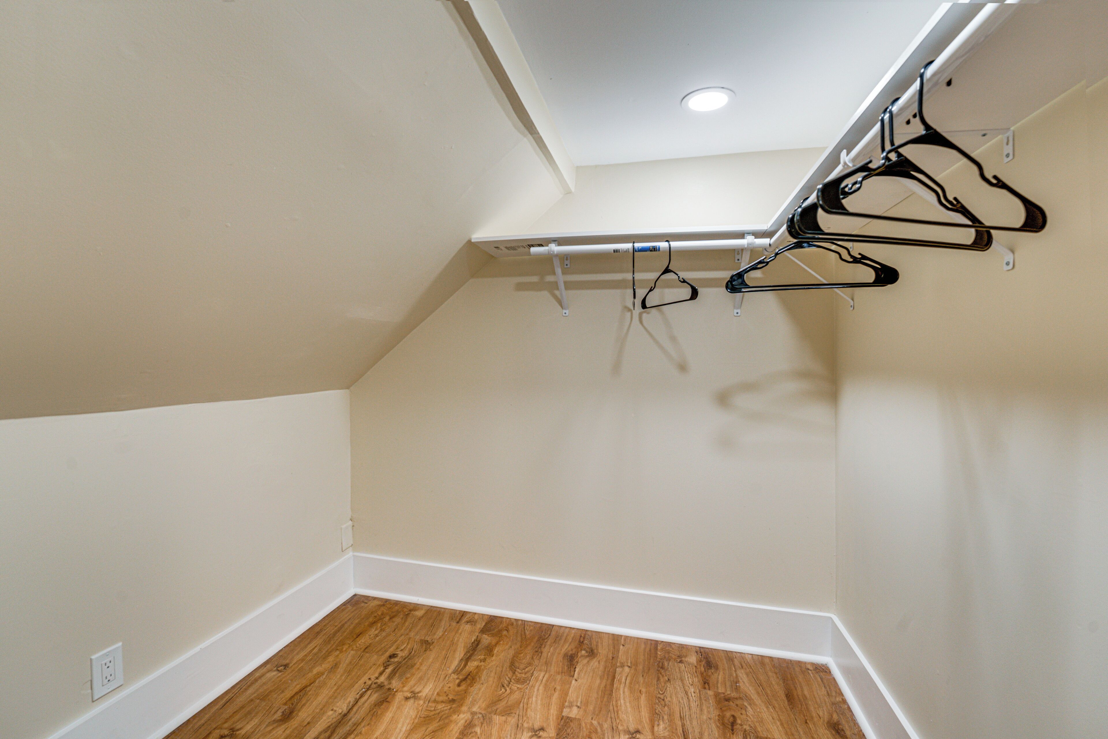 Una habitación con suelo de madera, techo inclinado y un tendedero con perchas.