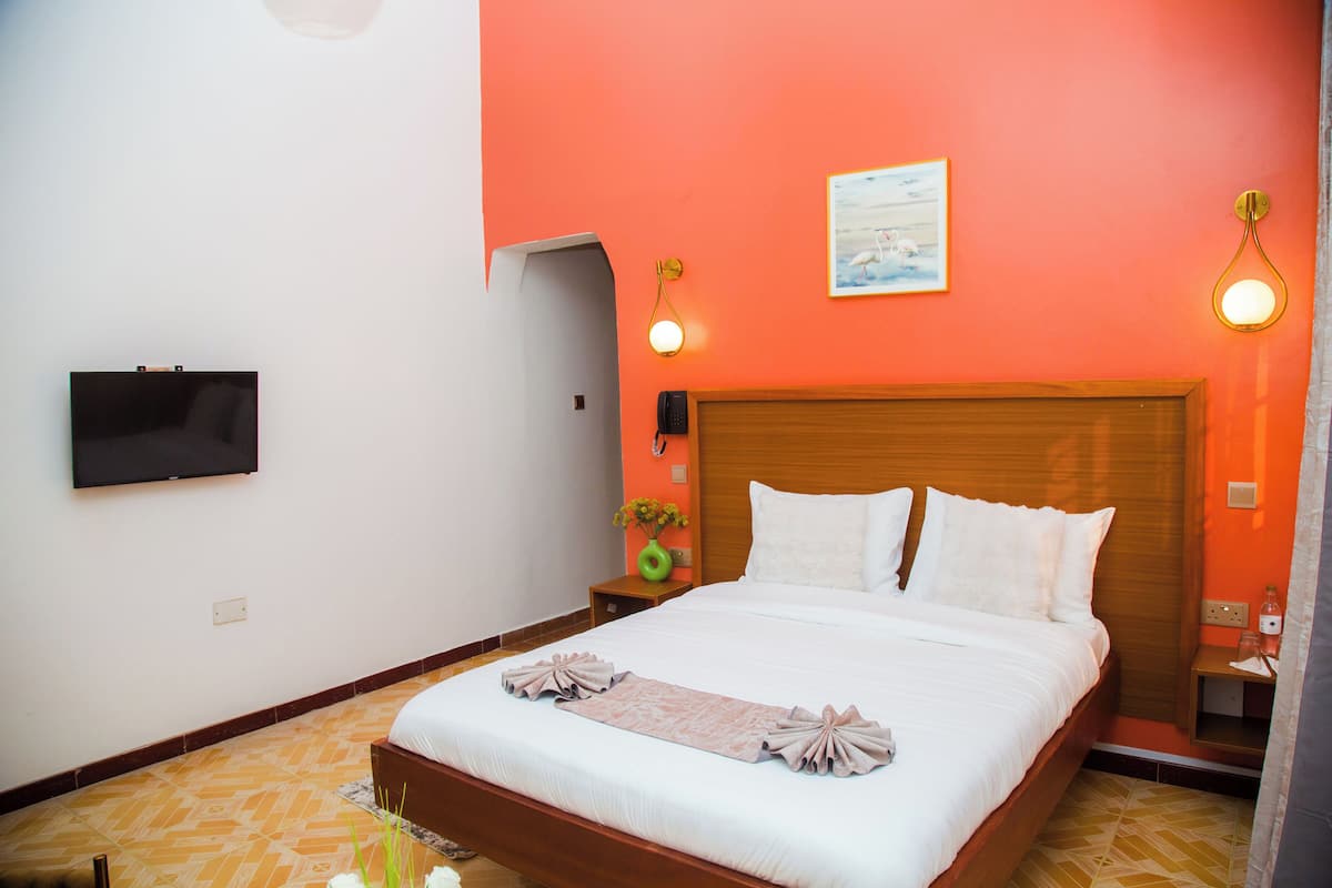 A hotel room with a large bed, a flat-screen TV, a wooden headboard, and a small bedside table with a vase of flowers.