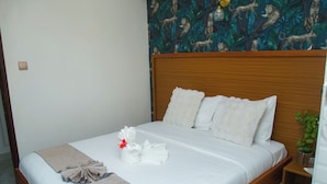 A neatly made bed with white linens and a beige throw blanket, a wooden headboard, and a tropical wallpaper pattern. - Whispering Palms Gardens (Nairobi)