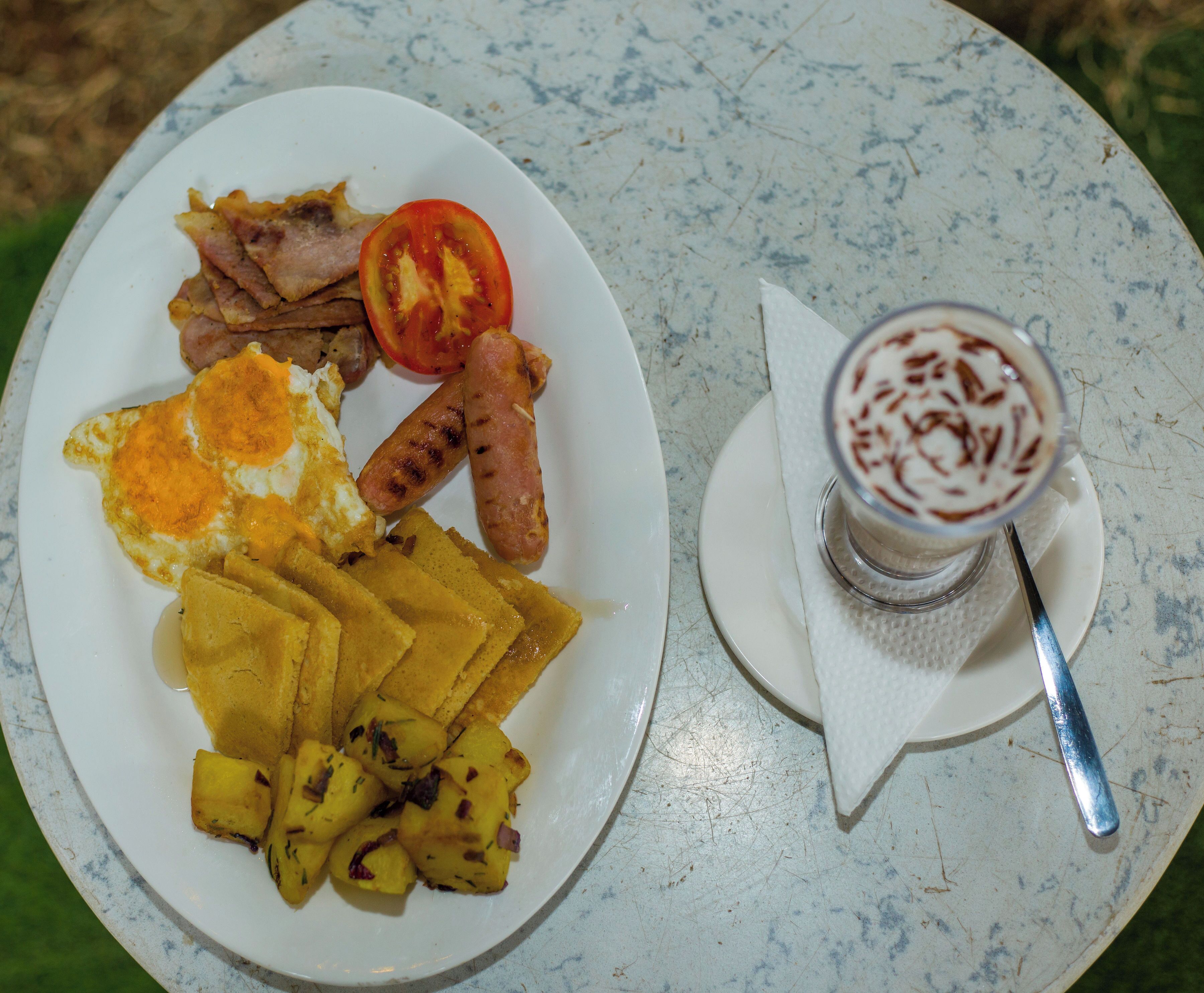 A plate with eggs, sausages, tomatoes, and potatoes, and a glass of a beverage with whipped cream and chocolate shavings.