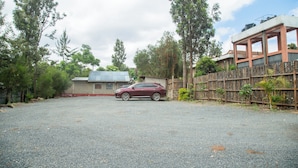 A red car parked in a gravel driveway with a wooden fence and trees in the background. - Whispering Palms Gardens (Nairobi)