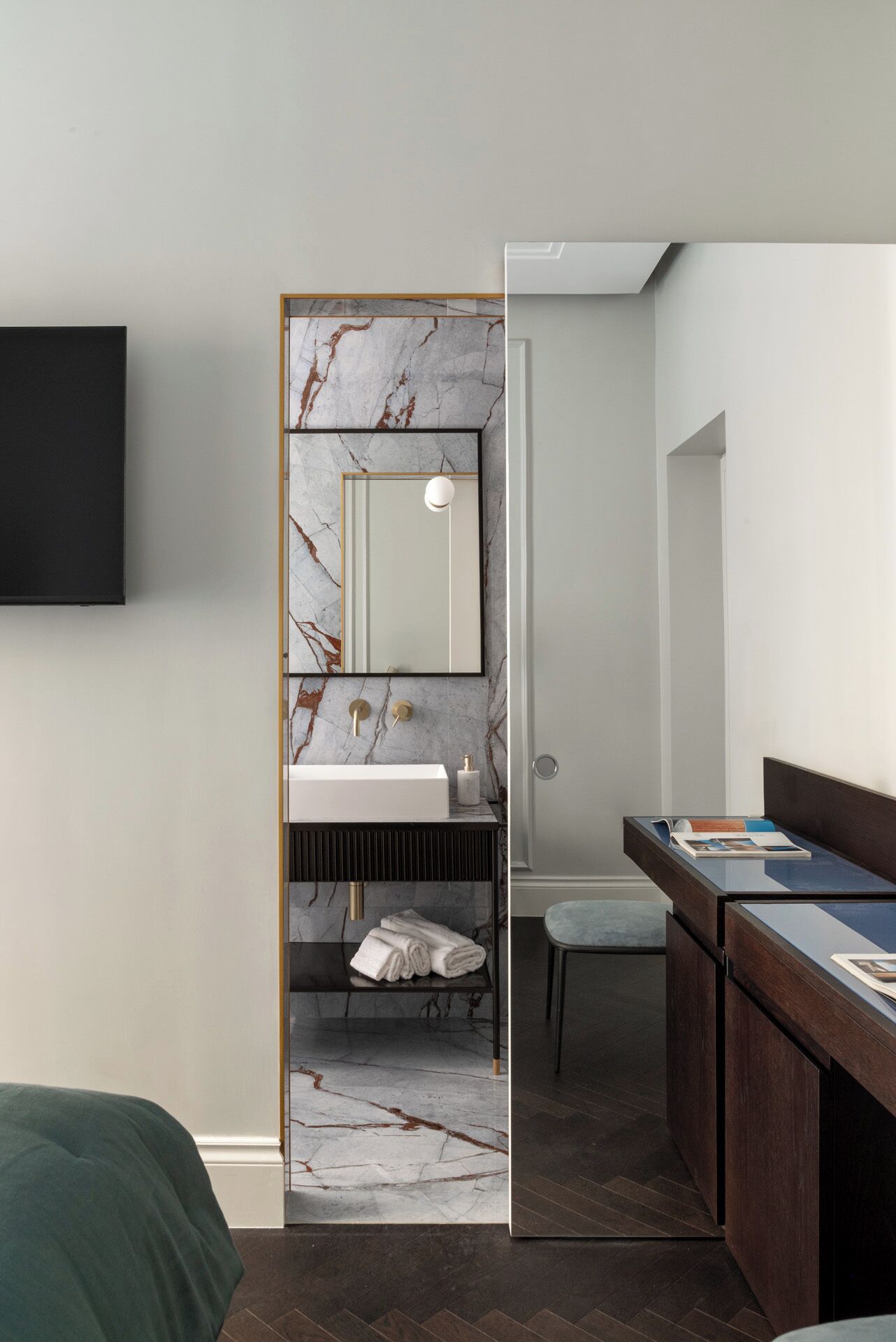 A modern bathroom with a marble backsplash, a white sink, a towel rack, and a wooden vanity with a magazine.