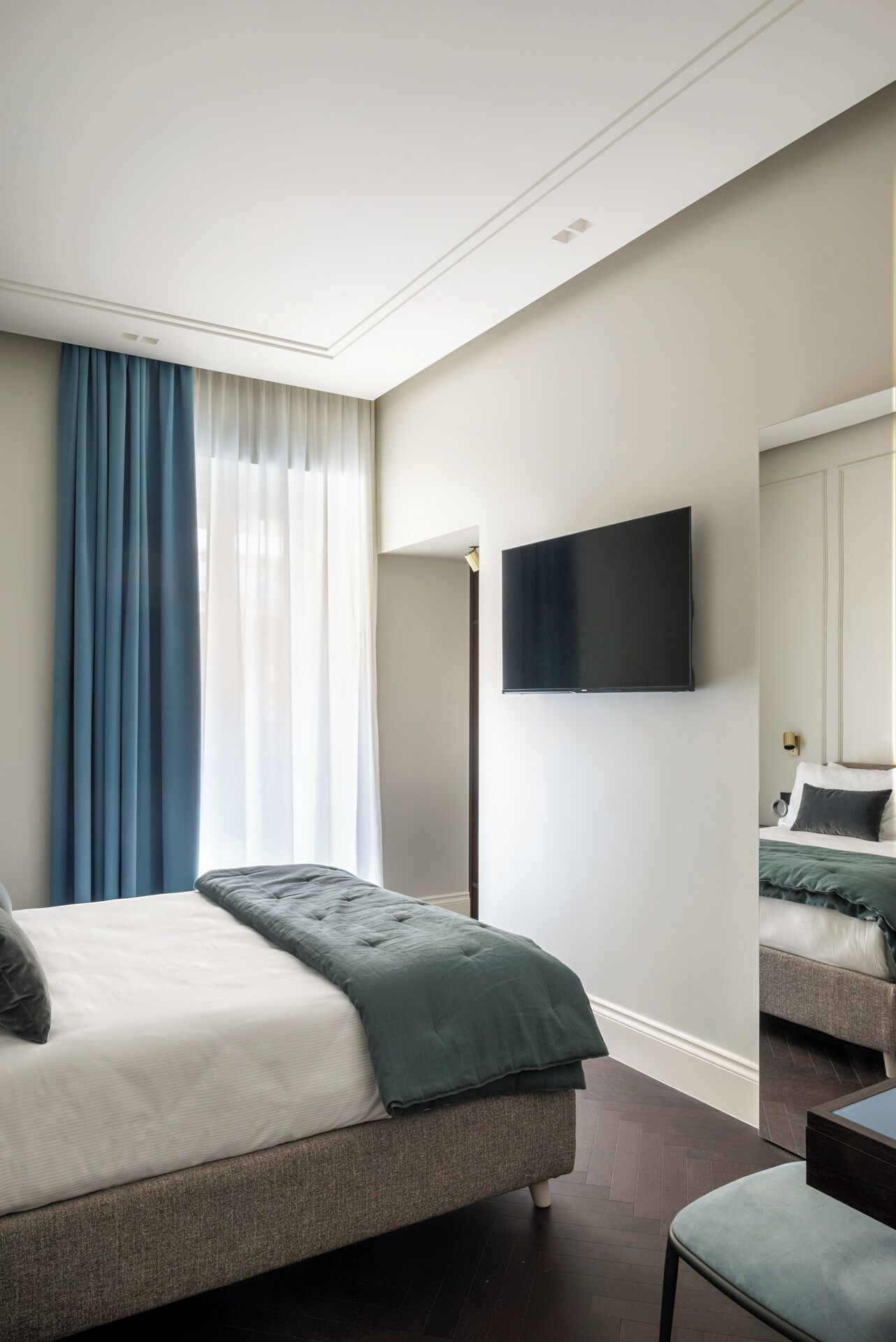 A modern bedroom with a large bed, a flat-screen TV mounted on the wall, and a separate seating area with a sofa.