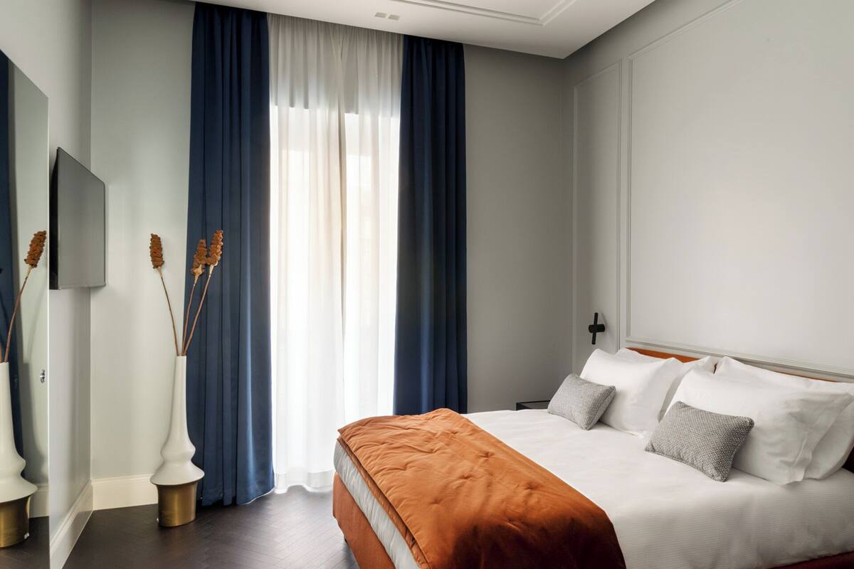 A hotel room with a large bed, a flat-screen TV, and a window with blue curtains.