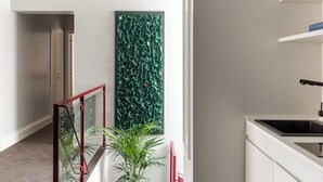 A modern interior with a staircase, a green textured wall, a potted plant, and a kitchen area. - Golden House Vatican - Regolo (Rome)