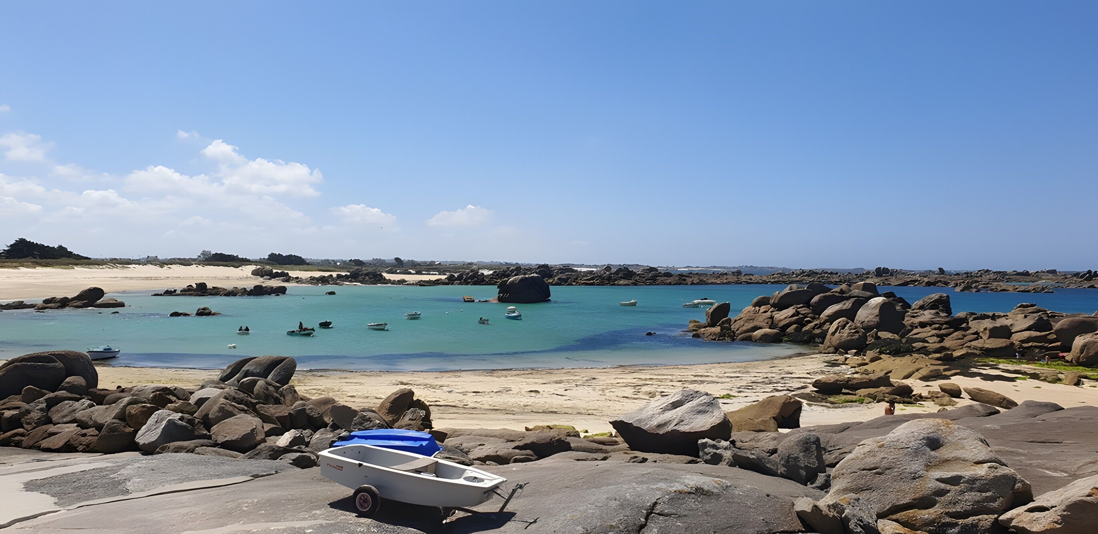Ein Strand mit einem Boot auf Felsen, ruhigem Wasser und weiter Küste.