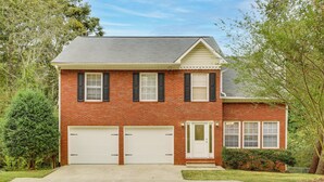 A two-story brick house with a white garage door, a front entrance with a small porch, and a well-maintained lawn. - Hike, Golf, Explore: Home 10 Mi to Lake Lanier! (Buford)