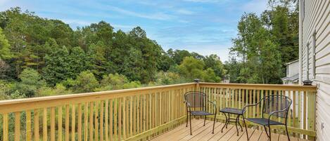 A wooden deck with two metal chairs and a railing overlooking a forested area.