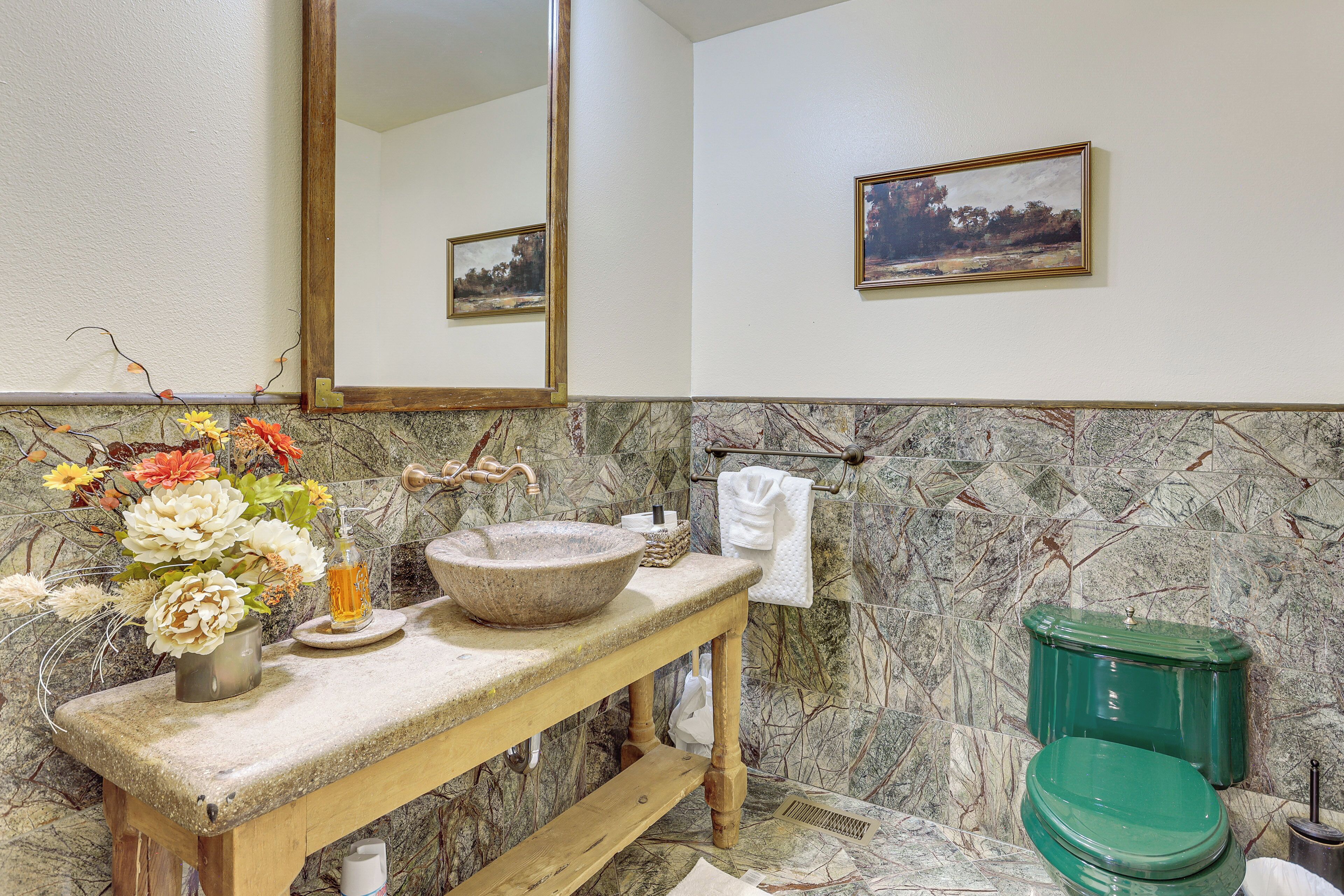 A bathroom with a marble wall, a wooden vanity, a green toilet, and a framed landscape painting.