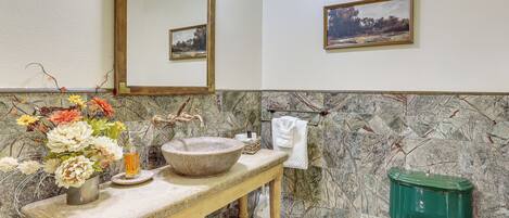 A bathroom with a marble wall, a wooden vanity, a green toilet, and a framed landscape painting.