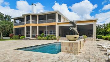 A modern two-story house with a swimming pool, outdoor seating, and a large decorative sculpture.