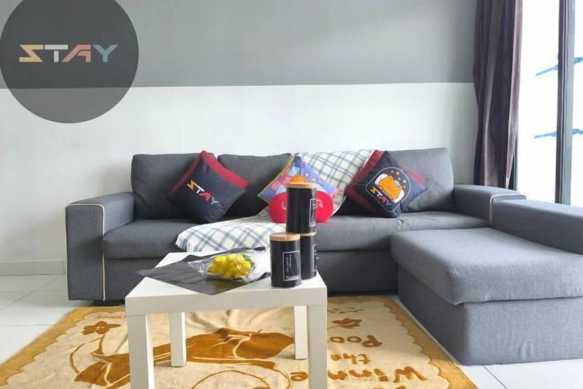 A grey sofa with patterned cushions, a white coffee table with a bowl and candles, and a rug with a floral design.