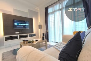 Een moderne woonkamer met een flatscreen televisie, een salontafel, een bank en een groot raam met gordijnen.