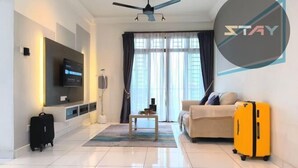 Une chambre d’hôtel moderne équipée d’un téléviseur à écran plat fixé au mur, d’un ventilateur de plafond, d’un canapé, d’une petite table et d’une valise jaune.