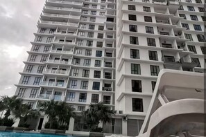 A multi-story hotel with balconies, a swimming pool, and palm trees. - Platino Paradigm Mall Homestay ByStay (Tebrau)