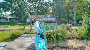 A wooden deck with a kayak, a covered area, and a house with a porch. - 13 Mi to South Haven: Lakefront Retreat w/ Dock! (Grand Junction)