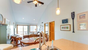 A kitchen with a large island, wooden dining table, and chairs. There is a ceiling fan, a sign on the wall, and framed pictures. - 13 Mi to South Haven: Lakefront Retreat w/ Dock! (Grand Junction)
